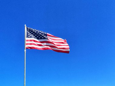 Bulutsuz mavi gökyüzüne doğru dalgalanan Amerikan bayrağının alçak açılı görüntüsü.