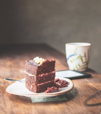 Kafe masasındaki e-okuyucu tabletinin yanında bir dilim çikolatalı pastanın dikey görüntüsü.