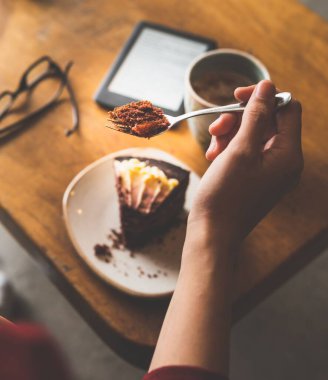 Kafe masasından kahve ve e-okuyuculu bir kek alırken çekilmiş dikey bir fotoğraf.