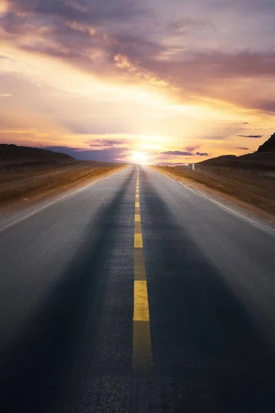 空の高速道路の垂直ショットカラフルな曇りの空と地平線に輝く太陽と日没 — ストック写真