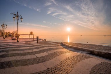 Lazise İtalya 'daki Garda Gölü' nün setinden gün batımı görüntüsü. Çizgili, düzensiz zemin ve ufukta güneş parlıyor.