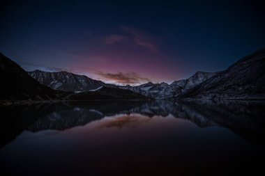 Geceleri dağlarla çevrili bir gölün büyüleyici görüntüsü.