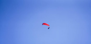 Mavi gökyüzünde kırmızı paraşütü olan bir paraglider.