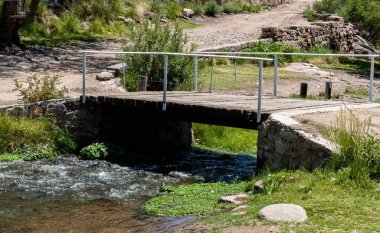 Güneşli bir günde nehrin üzerinden geçen küçük tahta köprünün yüksek açılı görüntüsü.