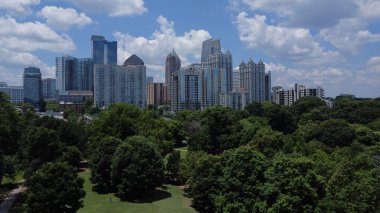 Atlanta 'nın ufuk çizgisi bulutlu bir gökyüzüne karşı park ve yeşil ağaçlar ön planda.