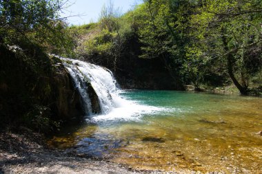 Şelale, güneşli bir günde Marche ormanındaki nehre akıyor.
