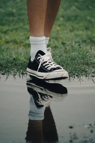 A vertical shot of a man\'s leg wearing a black sneaker stepping into a puddle