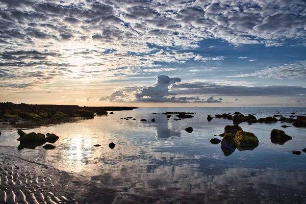 Vacker Stenig Strand Ett Reflekterande Hav Den Blå Molniga Himlen — Stockfoto