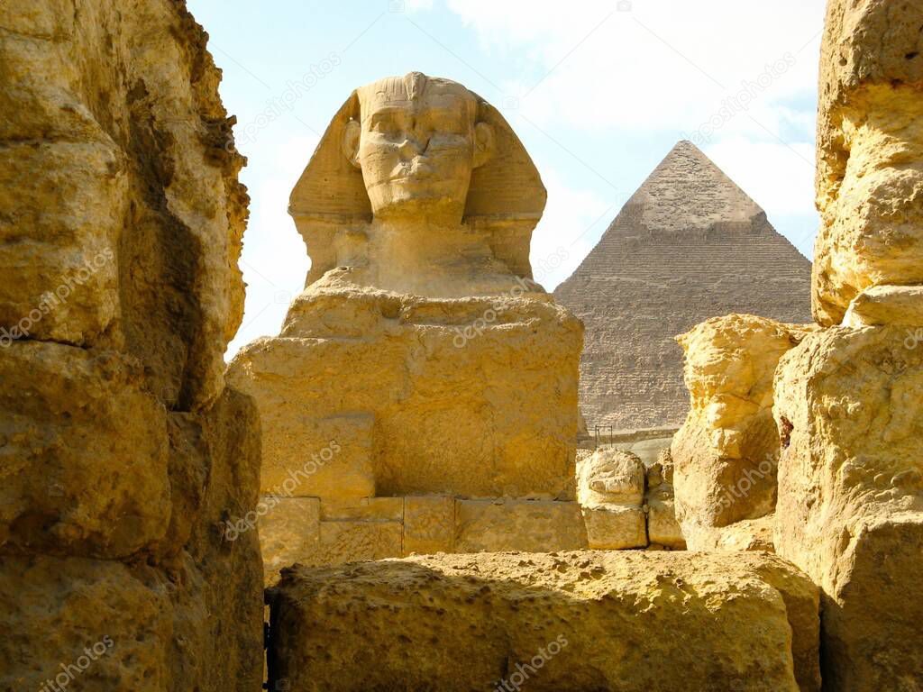 A closeup shot of the Sphinx from behind old rocks and the Great Pyramid of Giza in the background