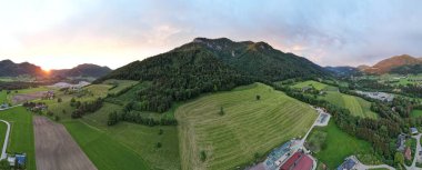 Dağ eteklerinde evleri ve ormanları olan bir tepenin havadan çekilmiş panoramik görüntüsü.