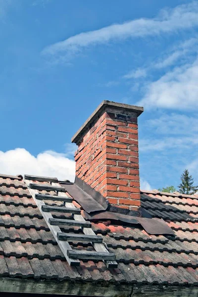 在蓝天的屋顶上有一个木制梯子的砖造烟囱的垂直视图 — 图库照片