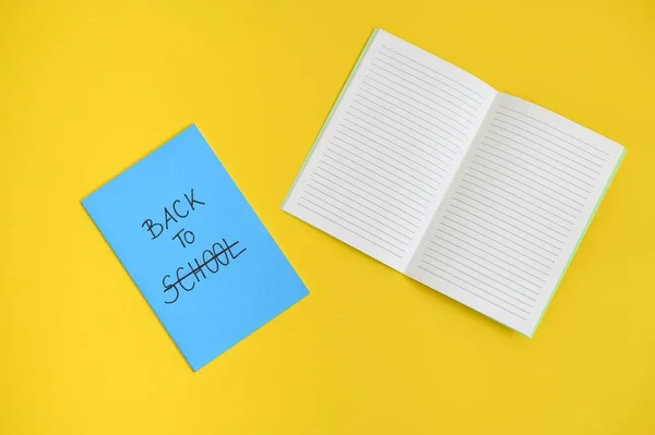 在蓝色笔记本的封面上写着返校的文字 打开的笔记本背景是明亮的黄色 — 图库照片