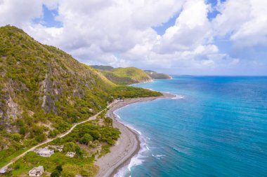 Plajı ve bulutlu arka planda kayalık dağları olan mavi bir deniz manzarası.