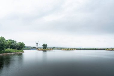 Kasvetli bir günde sakin göl kıyısındaki eski yel değirmeninin manzarası