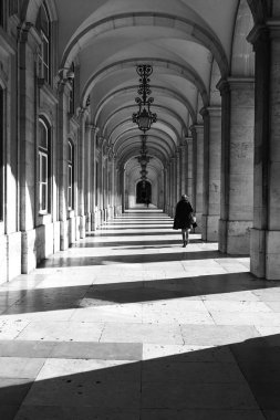 Eski bir kemer yolu koridorunun tek renkli bir görüntüsü. Işıksız fenerler ve arkadan geçen biri var.