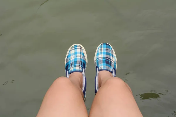 一只穿着帆布运动鞋坐在水面上一座木桥上的女孩脚的特写镜头 — 图库照片
