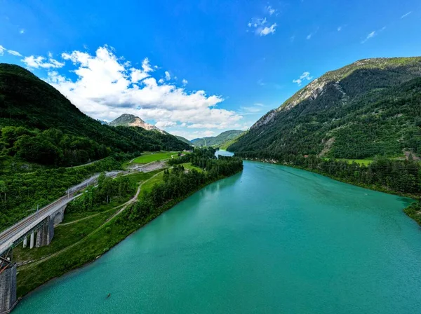 緑の山々の景色に対して紺碧の湖の上の橋の空中ショット — ストック写真