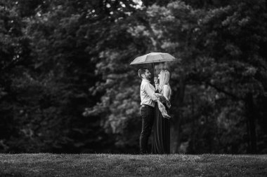 Takım elbiseli siyah-beyaz bir adam ve şemsiyesi altında şık elbiseli genç bir bayan.