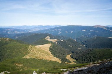 Güneşli bir günde mavi gökyüzünün altında yoğun çam ormanlarıyla kaplı katmanlı dağ sıralarının ve vadinin çarpıcı manzarası.