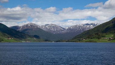 Norveç 'in Vestland şehrinde bulutlu bir günde sakin bir göl ve karlı dağlar manzarası.