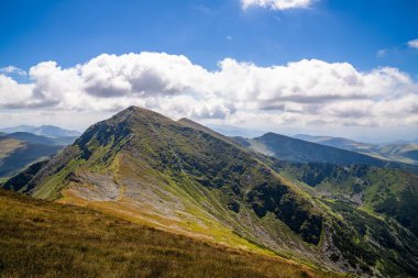 Sersemletici beyaz bulutlar ve mavi gökyüzü katmanlı dağ sıraları ve güneşli bir günde bitki örtüsüyle kaplı vadi üzerinde.
