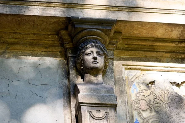 A woman face sculpture on the old weathered building facade.