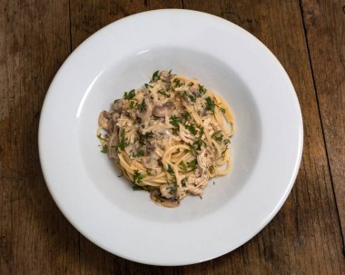 Tavuk, mantar, maydanoz ve beyaz tabakta parmesan peynirli makarna.