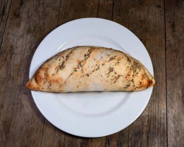 Calzone, ahşap arka planda beyaz plakalı.