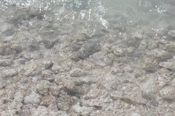 View of the transparent water in the shallow part of the sea with rocks in the background