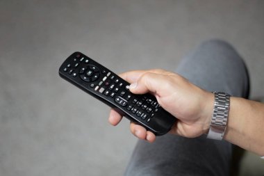 Elinde siyah bir televizyon kumandası olan bir el.