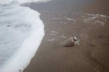İçinde kum olan cam bir şişe deniz kıyısına gömülmüş.