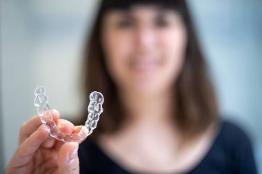 Gülümserken elinde görünmez diş hizalayıcısı tutan genç bir kadın.