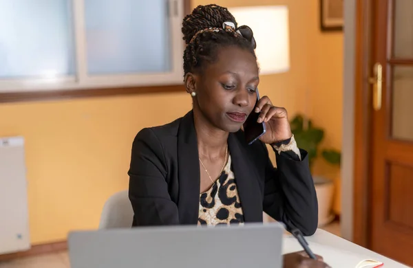portrait of Young black woman speaking on the phone with animal print top working with a laptop