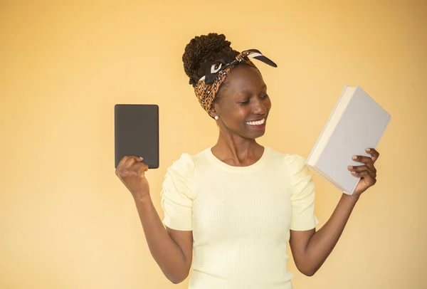 young woman comparing printed books to e-book while an e-book on her right hand while smilling at printed book on her left hand