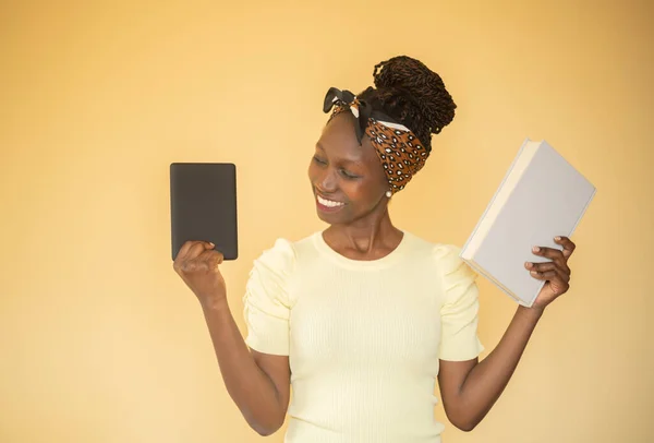 young woman comparing printed books to e-book while holding a book on her left hand while smilling at e-book on her right hand