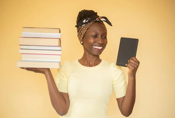 young woman comparing printed books to e-book while carrying books on her right hand while smilling at e-book on her left hand