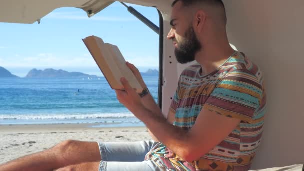 Молодой Путешественник Читает Книгу Фургоне Перед Красивым Пляжем Наслаждаясь Книгой — стоковое видео