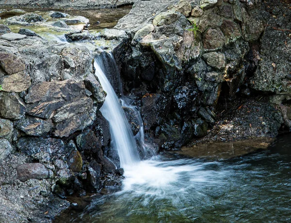 Flowing waterfall over rocks to a small pnd