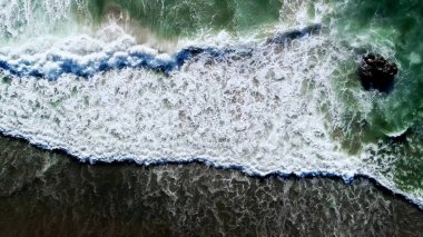 Deniz dalgaları kumlu plaja çarpıyor.