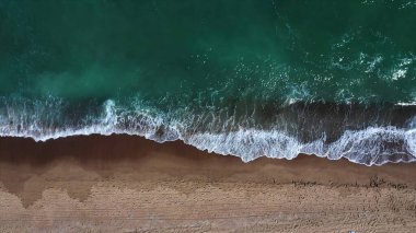 Deniz dalgaları kumlu plaja çarpıyor.