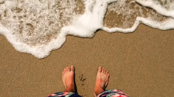 Legs of a man on a sandy beach near the sea waves