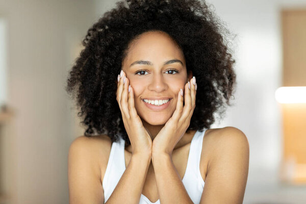  African american woman touching face with perfect smooth skin standing in bathroom
