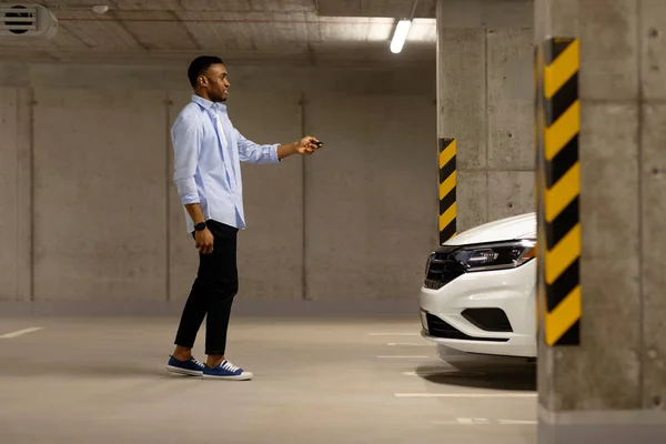 African american man with car keys in front of car in underground parking. High quality photo