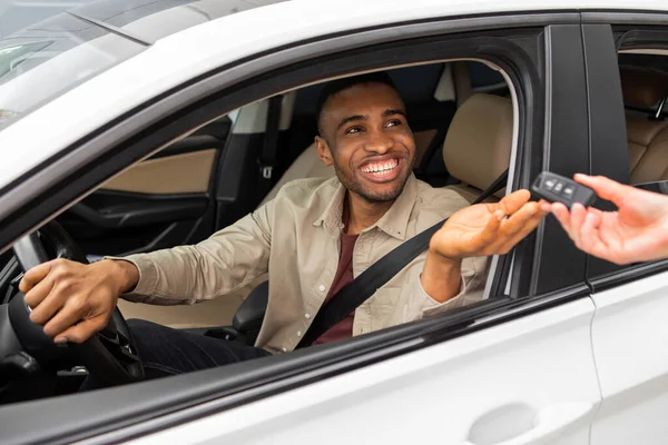 Test drive of a new car. Young black man grabs the car keys while sitting in the drivers seat. High quality photo