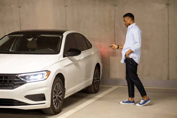 African american man opens his car with keys in an underground parking lot while talking on the phone. High quality photo