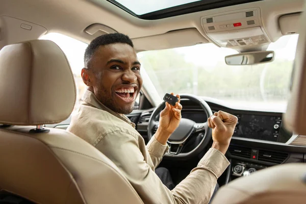 Joyful african american guy holding auto key shaking fists sitting in automobile . High quality photo