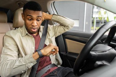 Afrika kökenli Amerikalı bir adam arabada sinirli bir ifadeyle kol saatine bakıyor. Yüksek kalite fotoğraf