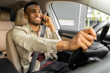 Araba kullanırken gülümseyen, telefonla konuşan, akıllı telefon kullanan Afro-Amerikan bir adam. Yüksek kalite fotoğraf