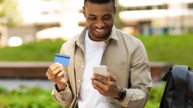 Afrikalı genç adam dışarıda akıllı telefon kullanarak online alışveriş yapıyor. Yüksek kalite fotoğraf