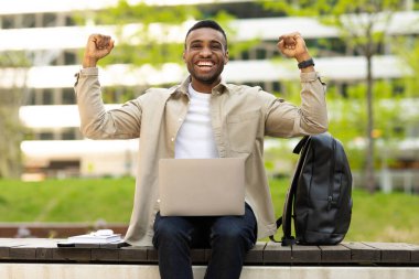 Şehirde bir bankta otururken yumruklarını sallayarak zaferi kutlayan mutlu siyah adam. Yüksek kalite fotoğraf